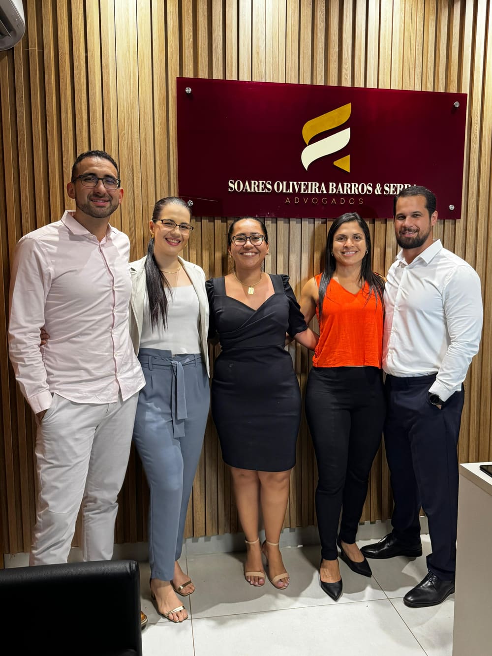 Equipe em frente à placa do escritório, na recepção de madeira ripada